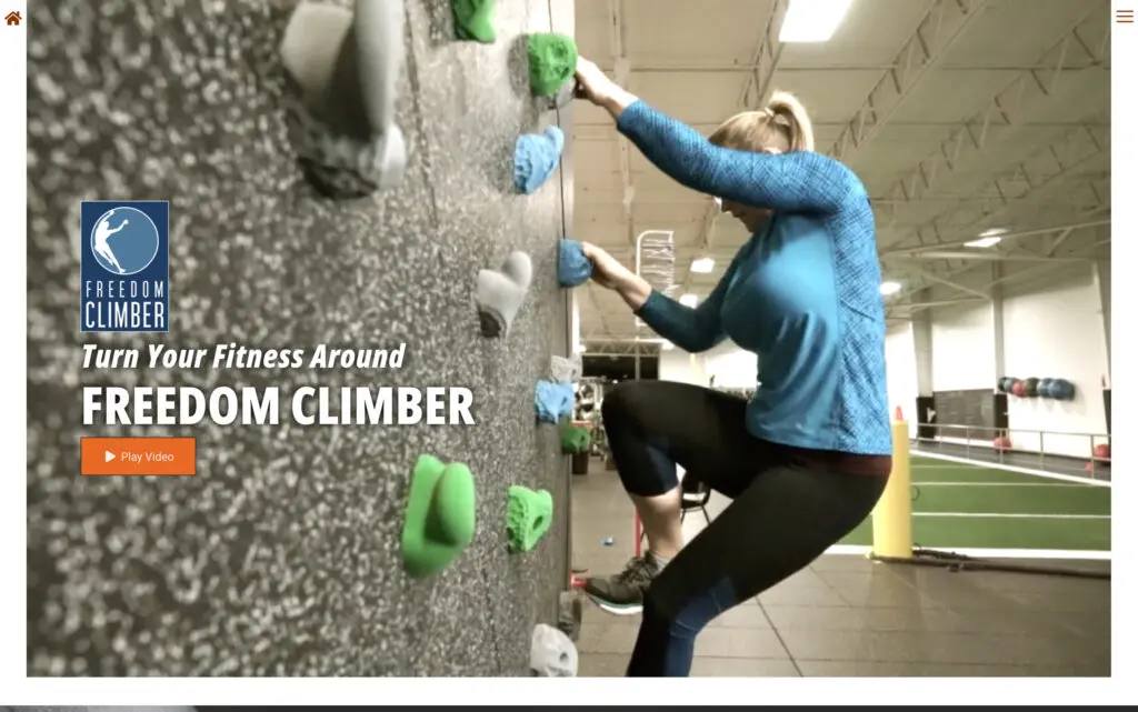 Woman climbing on a Freedom Climber wall, showcasing an innovative fitness method. The indoor setting features colorful climbing holds and gym equipment in the background, emphasizing a unique approach to exercise and strength training.